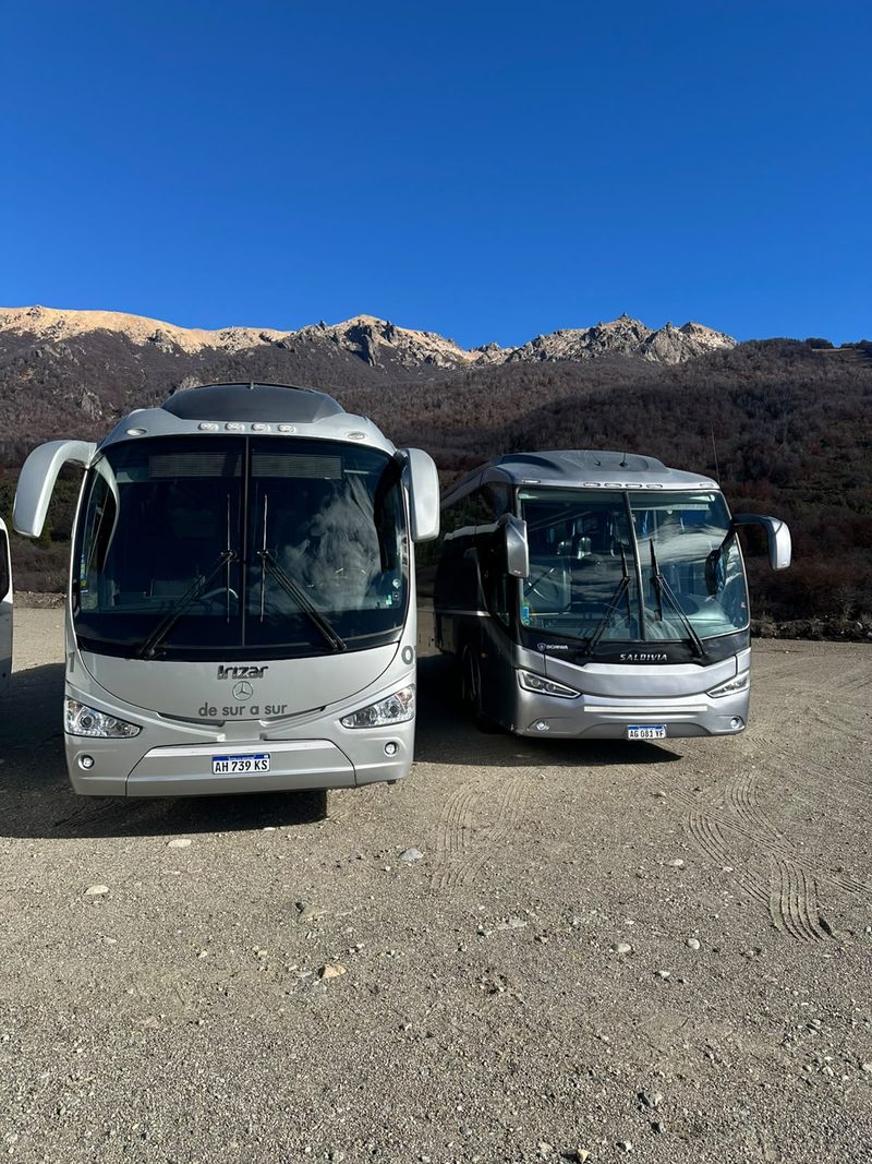 Dos buses de De Sur a Sur, de frente, con la montaña de fondo